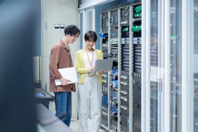 Two IT professionals in a data center collaborating in front of server racks with a laptop.