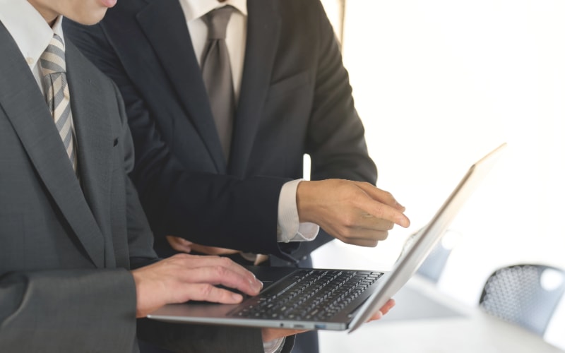 Two business professionals in suits looking at and pointing to a laptop screen