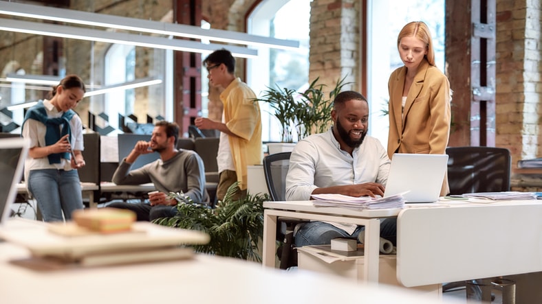 Coworkers collaborating around a laptop in a modern open-plan office